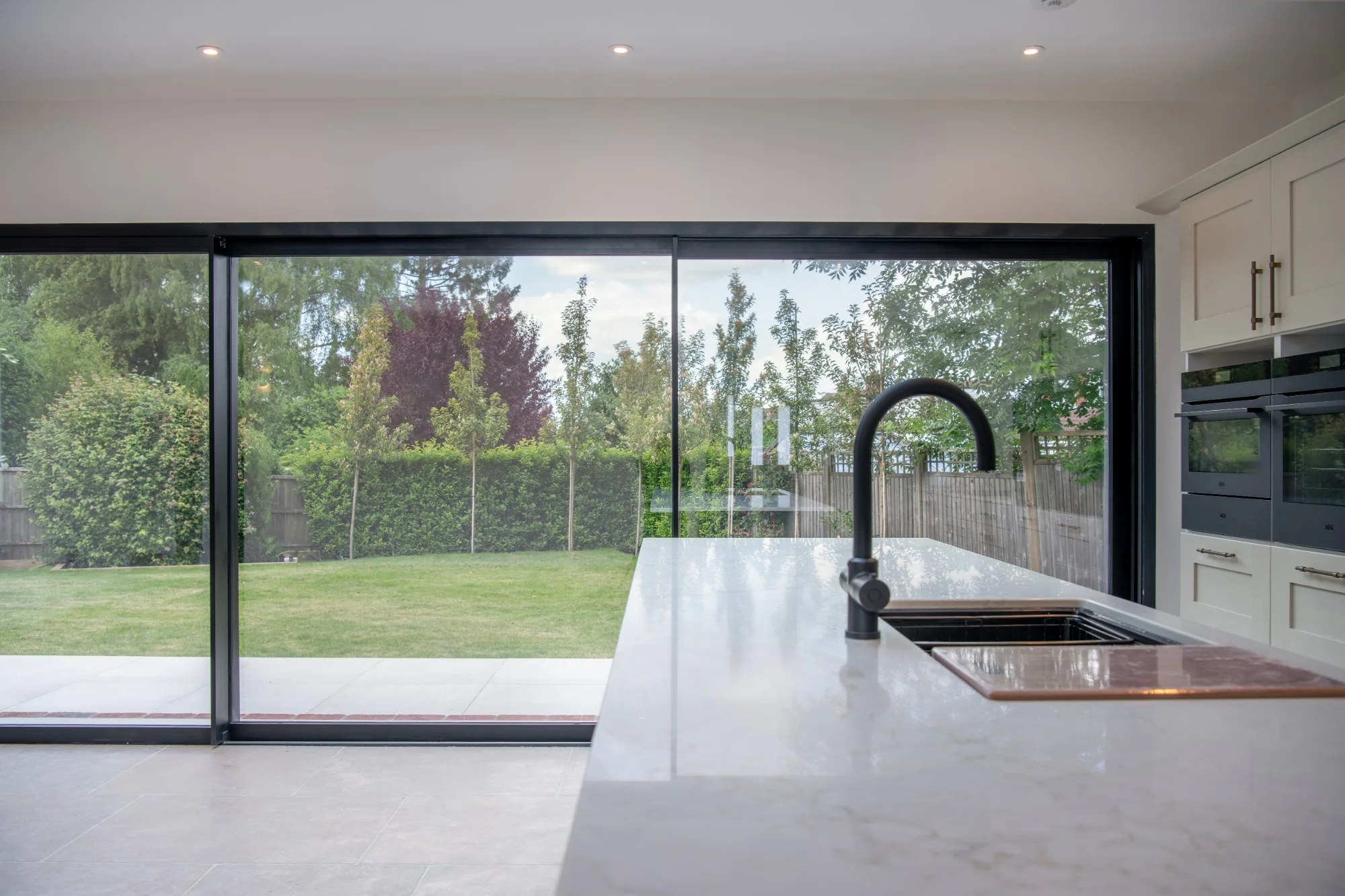 Looking from the kitchen island at the Willows, across a marble worktop and through full-width glazing to the garden